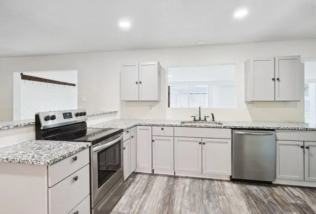 Modern open kitchen with white cabinets, stainless steel appliances, large island with bar stools, and pendant lights.