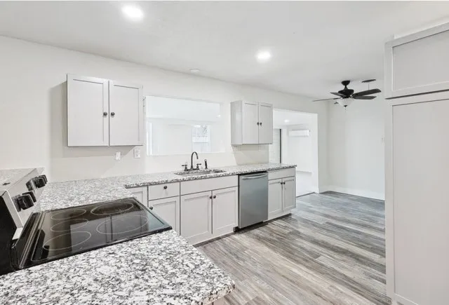 Modern open kitchen with white cabinets, stainless steel appliances, large island with bar stools, and pendant lights.