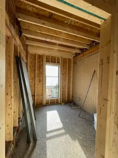 Partially constructed room with exposed wooden beams, unfinished walls, and construction materials scattered on the floor.